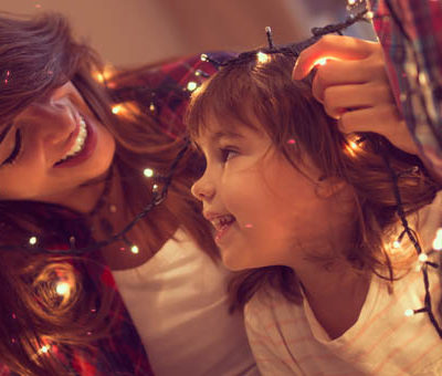 A picture of a woman smiling to a girl, wrapped in Christmas lights