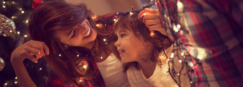 A picture of a woman smiling to a girl, wrapped in Christmas lights
