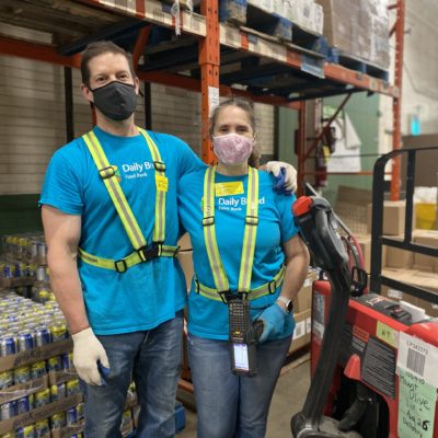 A picture of a man and a woman in a warehouse, wearing masks, and hugging