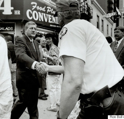 A picture of a crowded street with a man in uniform facing away, shaking hands with a man in a suit