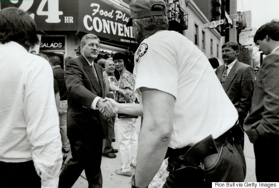 A picture of a crowded street with a man in uniform facing away, shaking hands with a man in a suit