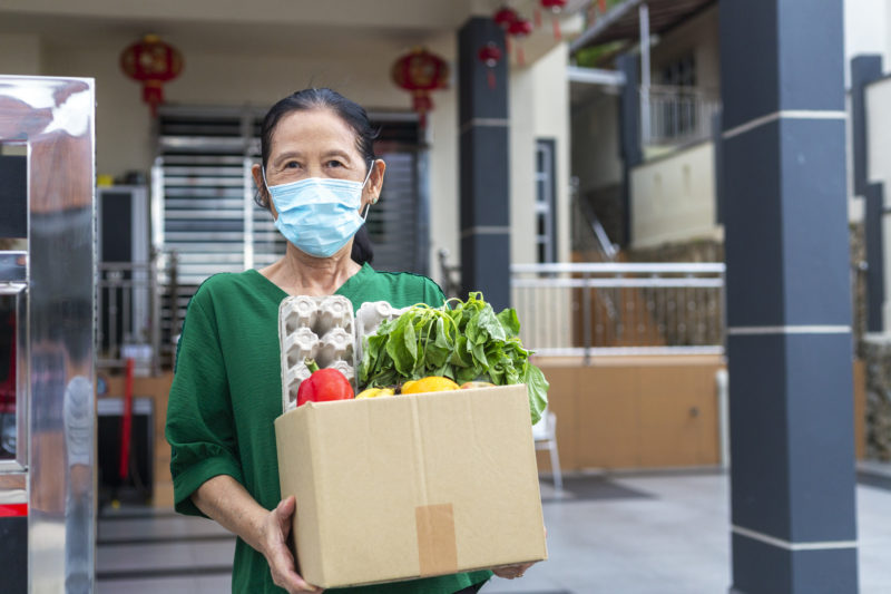 Portrait of senior Asian woman wearing face mask received crate of food during pandemic