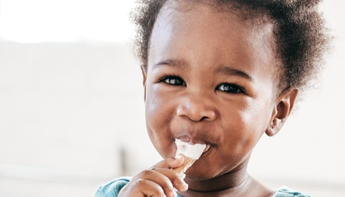 A small Black child eating yoghurt with a big smile on their face.