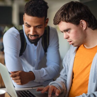 Two men, one with Down Syndrome, look at a computer. Food banks provide even more than food to their communities.