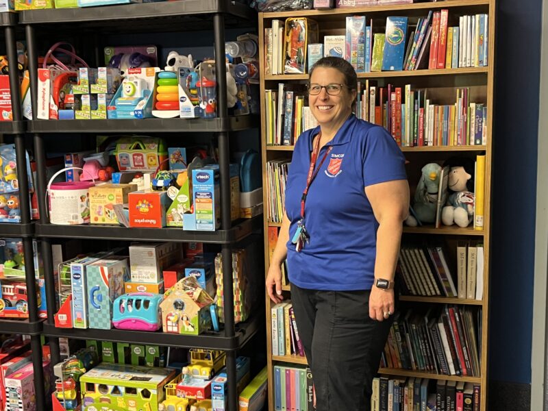 A woman standing in front of a shelf of toys and a bookshelf at a food bank.