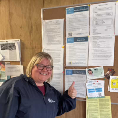A woman smiling and pointing at a bulletin board with information about ARC.