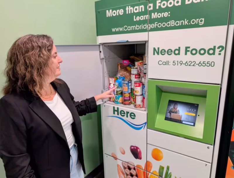 A woman stands in front of a Feed Ontario funded pick up locker filled with food.