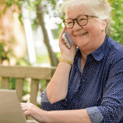 An older woman considers leaving a planned gift in front of her computer, smiling.