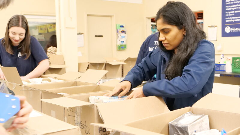 Two women reach into boxes while volunteering at a food bank.