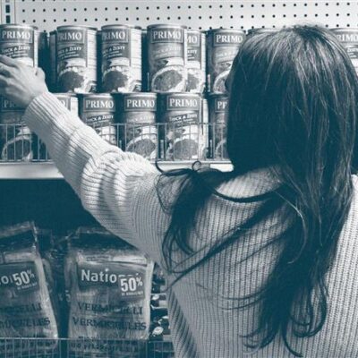 Image en noir et blanc d'une femme attrapant une boîte de conserve sur une étagère.