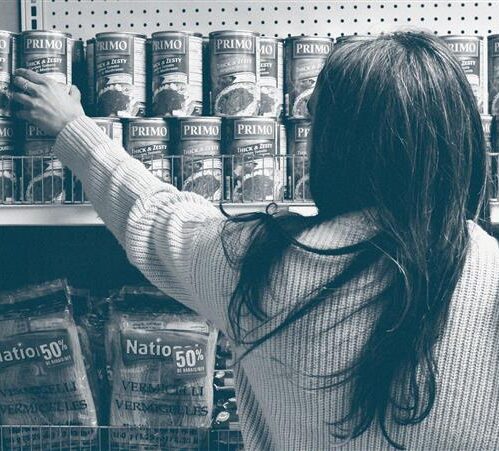 Image en noir et blanc d'une femme attrapant une boîte de conserve sur une étagère.