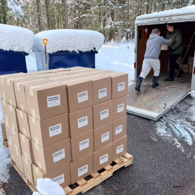 A person passes an emergency food box to someone in a truck, behind a pallet of food hampers being distributed during a snow storm.