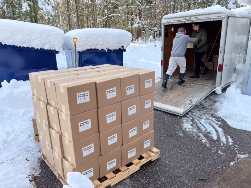 Une personne passe une boîte de nourriture d'urgence à une autre personne dans un camion, derrière une palette de paniers de nourriture distribués lors d'une tempête de neige.