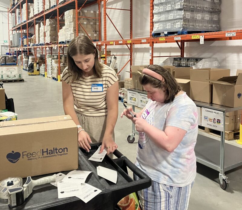 Two people stand beside boxes they're labelling.