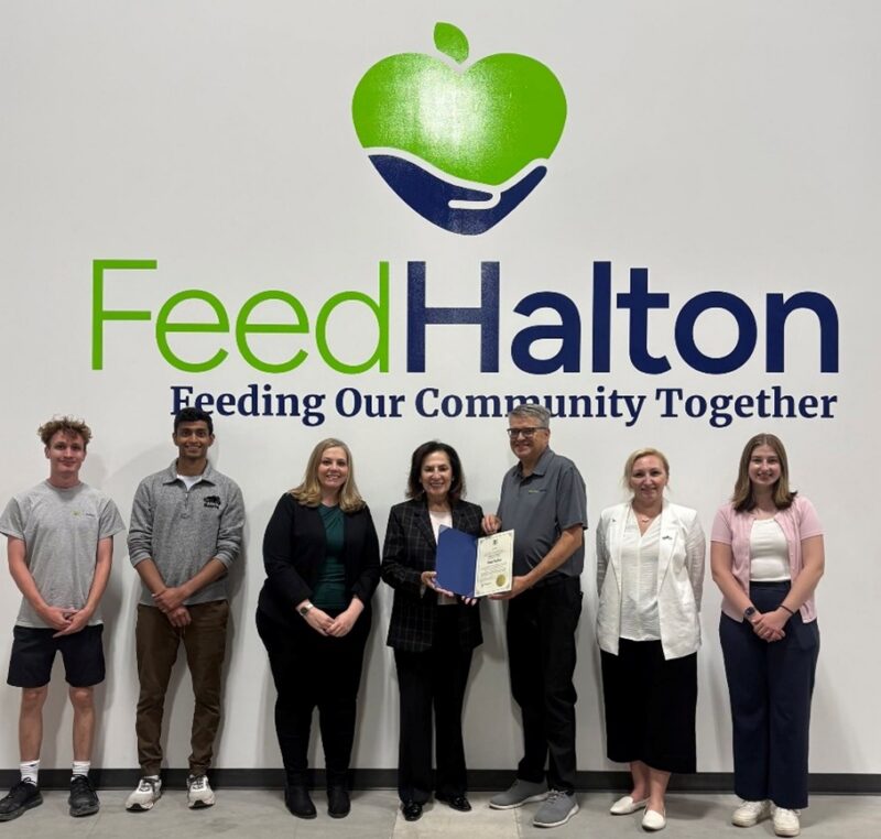 A group of people stand beneath FeedHalton's logo.