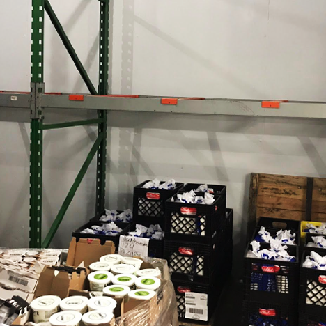 Industrial storage room with crates and pallets on shelves and stacked on the floor, filled with various goods including boxes and containers.