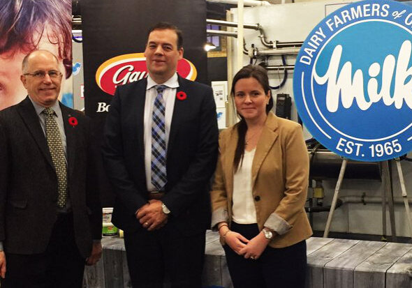 Three people stand in front of Dairy Farmers of Ontario and Ontario Food Banks banners at an event, with a cow displayed on the left.