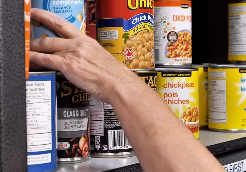 A hand reaching to grab a canned good from a food bank shelf in Ontario.