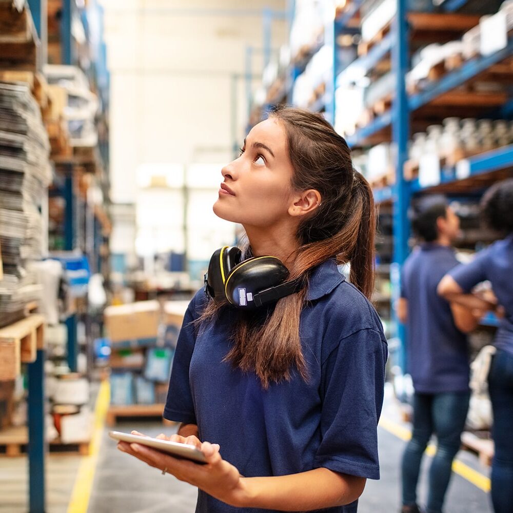 A picture of a woman holding a notepad looking at shelves in a warehouse